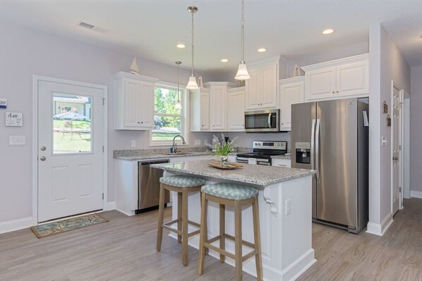 A modern kitchen with white cabinetry, stainless steel appliances, and a central island with bar stools.