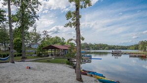 A beach with a covered pavilion, kayaks, and a calm lake.