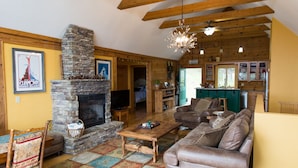 A cozy living room with a stone fireplace, wooden beams, a sofa, and a television. - Cozy mountain log chalet overlooking the slopes of Hatley Pointe Ski Resort.  (Mars Hill)