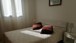 En snyggt bäddad säng med ett mönstrat överkast och två kuddar, ett sängbord med en lampa och en inramad tavla på väggen.