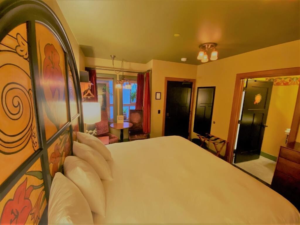 Ein Hotelzimmer mit einem großen Bett, einem Schreibtisch mit Stuhl, einem kleinen Tisch und einem Spiegel.