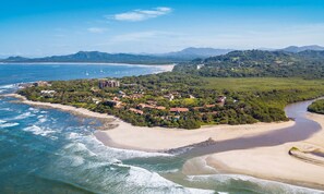 Luchtbeeld van een kustplaatsje met een strand, huizen en bergen op de achtergrond.