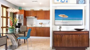 A modern kitchen with wooden cabinets, a glass dining table, and a large painting of a beach scene. - Agua Azul by Island Properties Online (Lowlands)