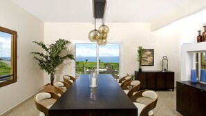 A modern dining area with a long table, multiple chairs, a decorative plant, and a view of the outdoors. - Artimino by Island Properties Online (Lowlands)