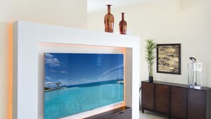 A living room with a large flat-screen TV mounted on a white wall, a dark wooden cabinet below, and a framed artwork to the right. - Artimino by Island Properties Online (Lowlands)