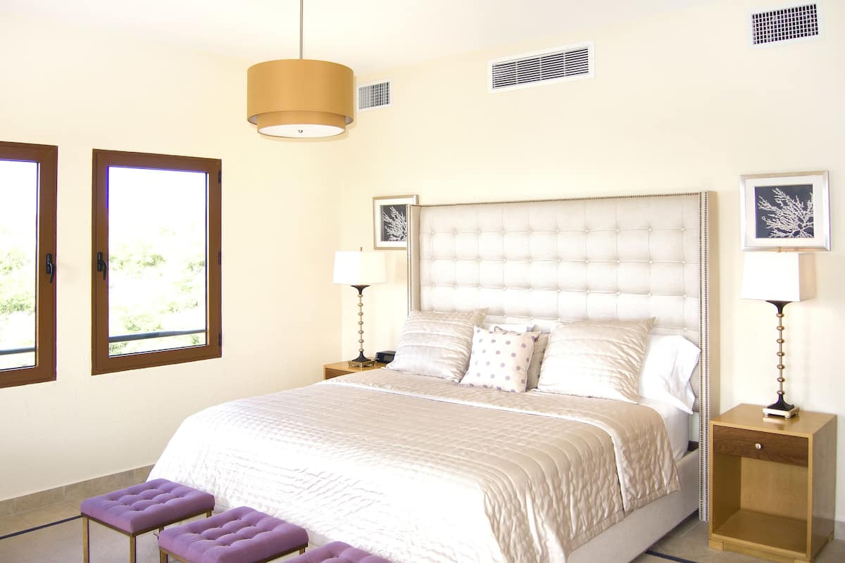 Quarto bem arrumado com uma cama grande, duas mesas de cabeceira, um lustre e duas janelas.