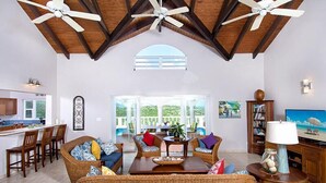 Uma sala de estar ampla, com teto alto, ventoinhas no teto embutidas, uma grande janela e vista para o exterior.