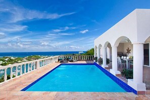 Une piscine avec vue sur l’océan, un patio couvert et un bâtiment blanc orné d’arcades.