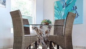 Uma área de refeições com cadeiras de vime e uma mesa de vidro, uma janela com vista e um quadro na parede.