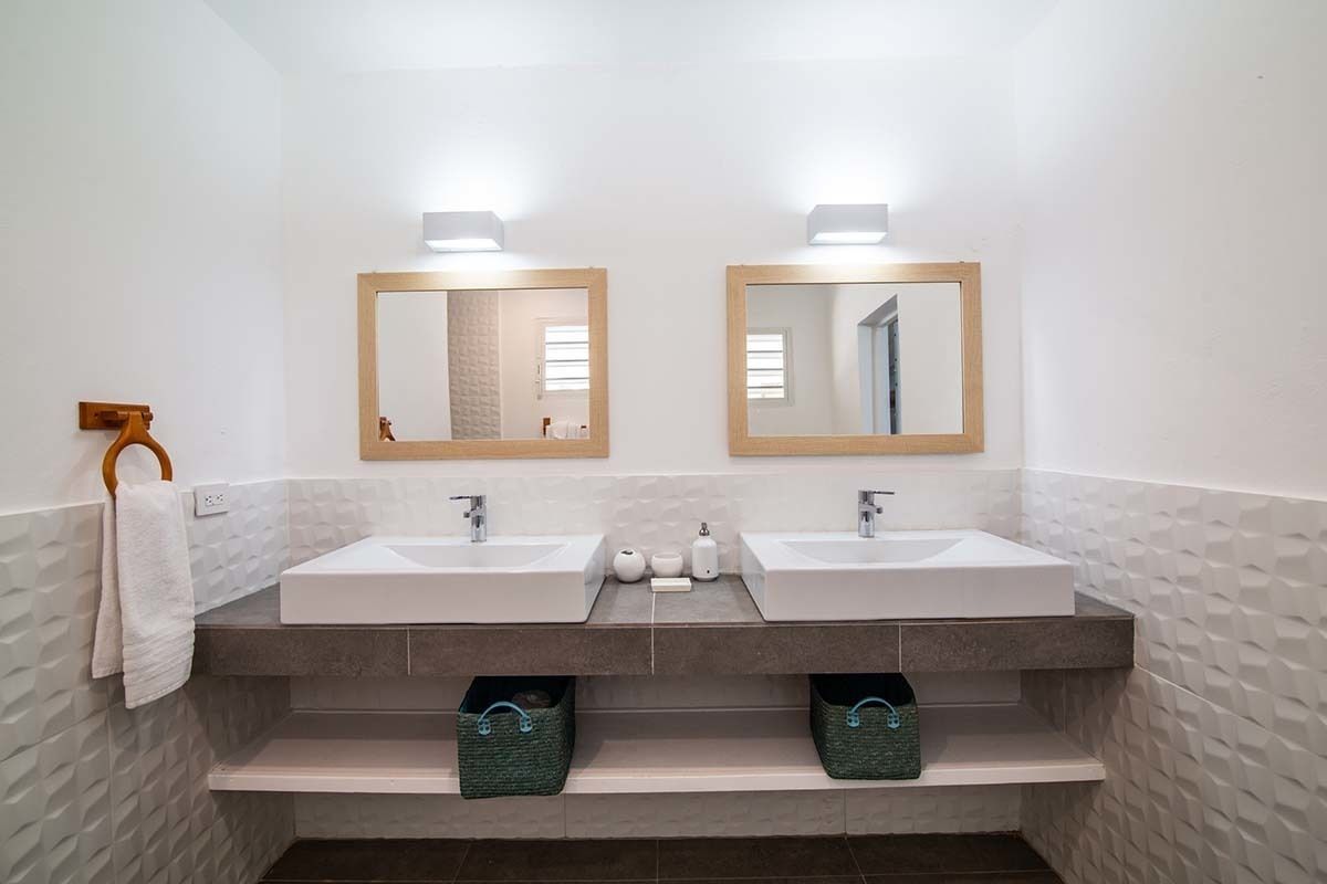 Baño con dos lavamanos, un perchero y dos espejos.