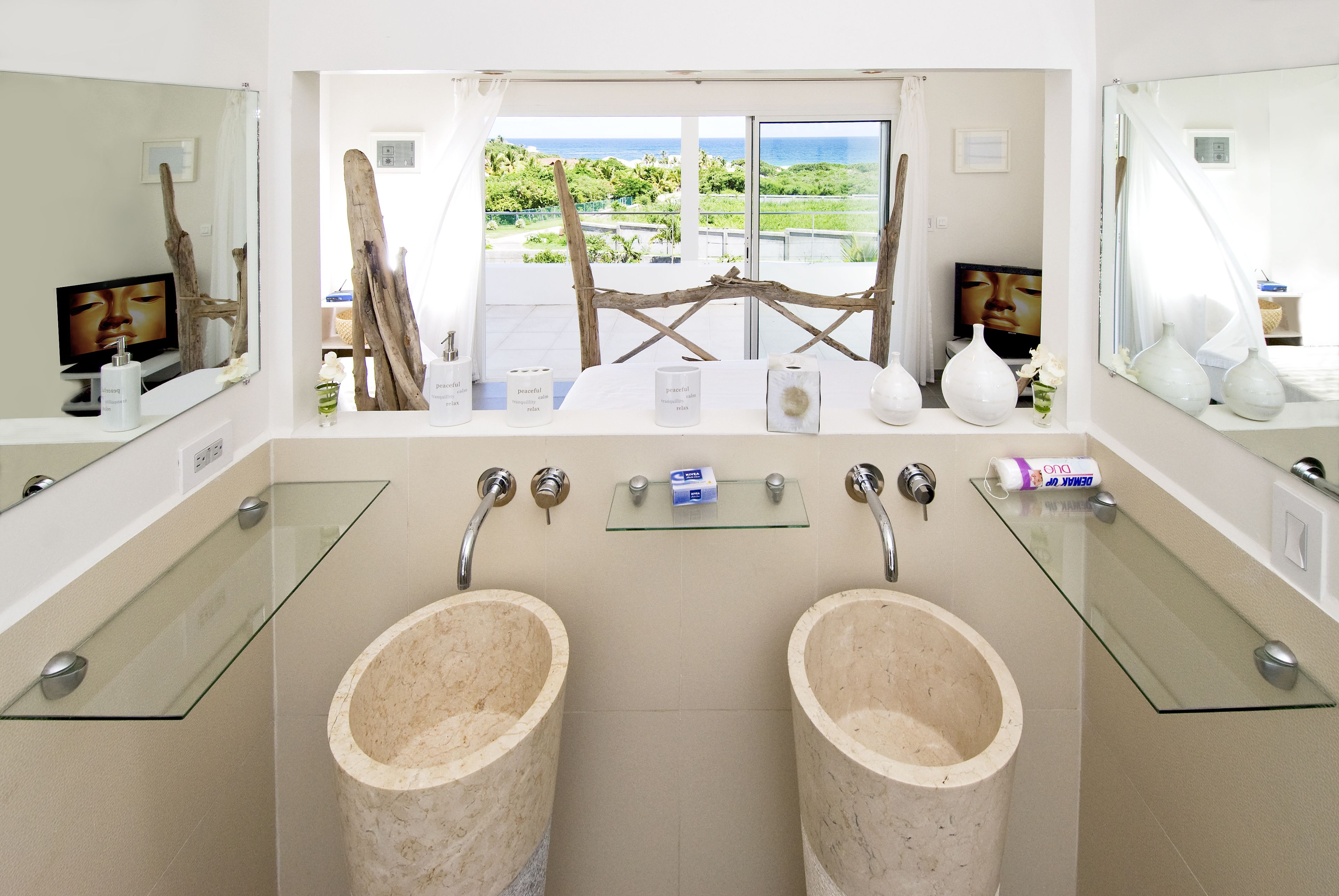 A bathroom with two marble sinks, a glass shelf, and a view of the ocean.