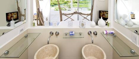Un bagno con due lavabi in marmo, uno scaffale in vetro e vista sull'oceano.