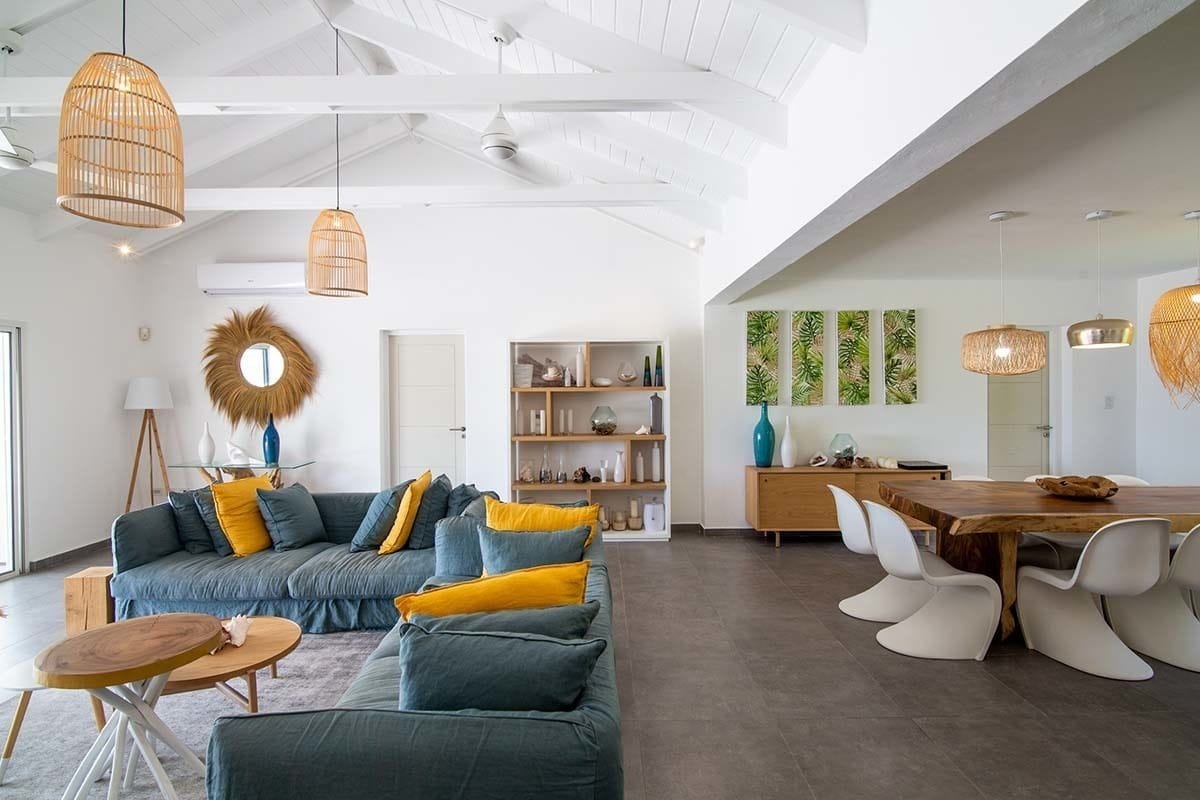 A modern living room with a sectional sofa, a wooden dining table, and white chairs.