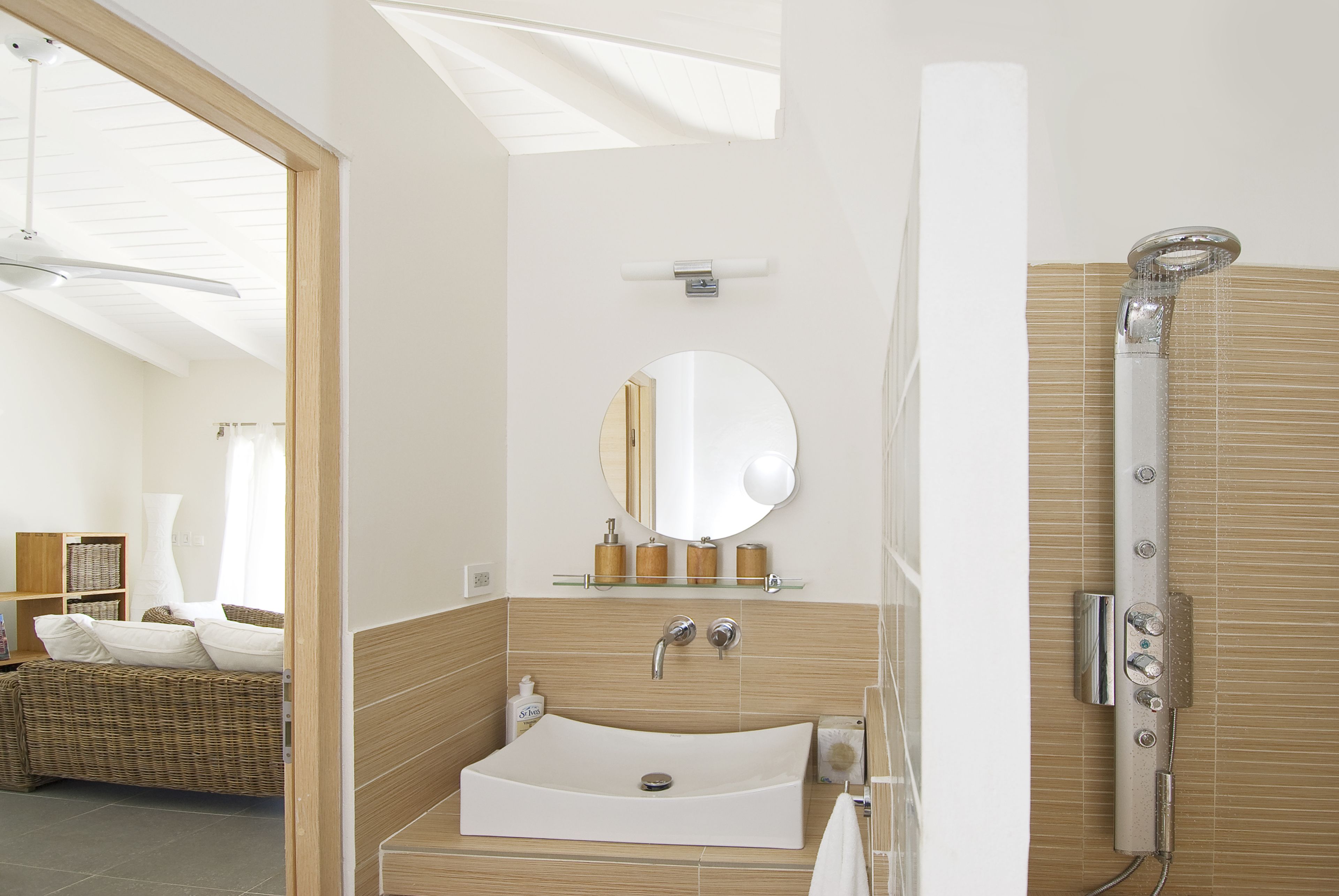 Un baño moderno con una bañera independiente, un espejo grande y un sofá de mimbre en la habitación contigua.