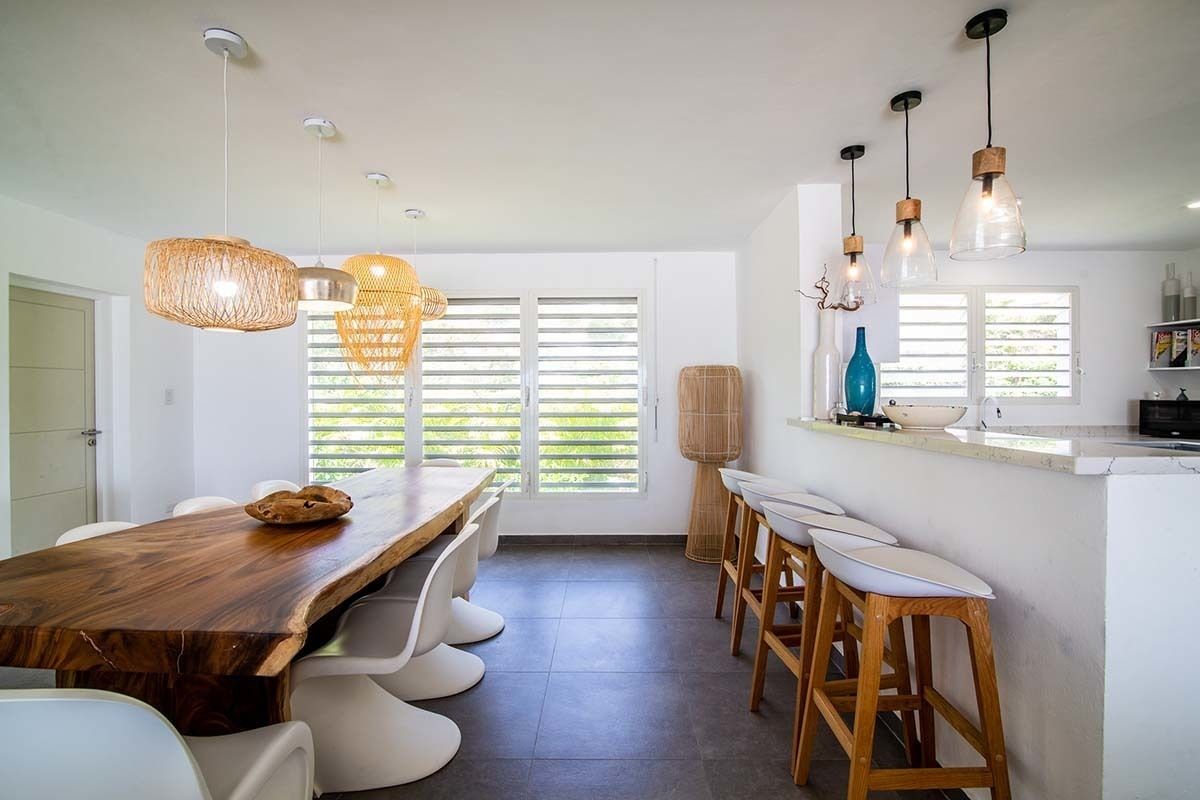 Una cocina moderna con una mesa de comedor de madera, taburetes de bar blancos y luces colgantes.