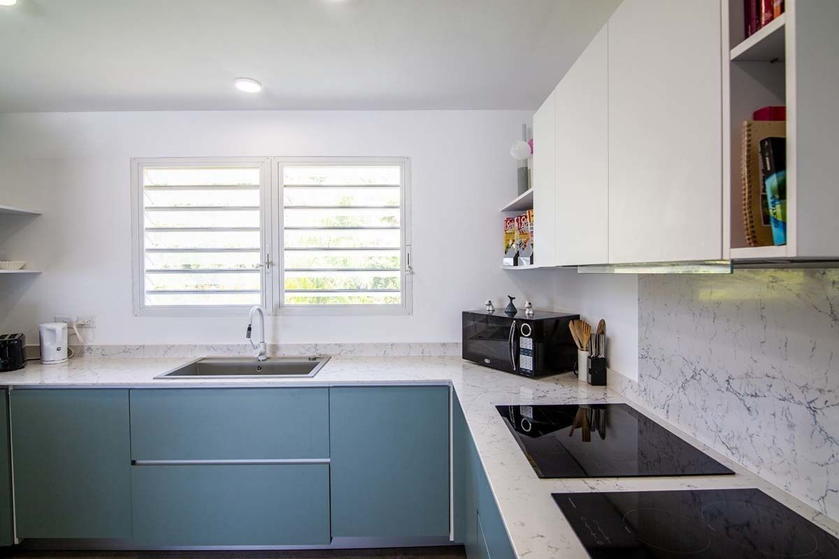 A modern kitchen with a double sink, a microwave, and a built-in oven. There is a window with blinds, a countertop with a kettle, and a cabinet with kitchen utensils.