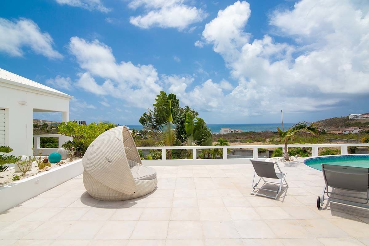 A rooftop terrace with a pool, lounge chairs, and a view of the sea.