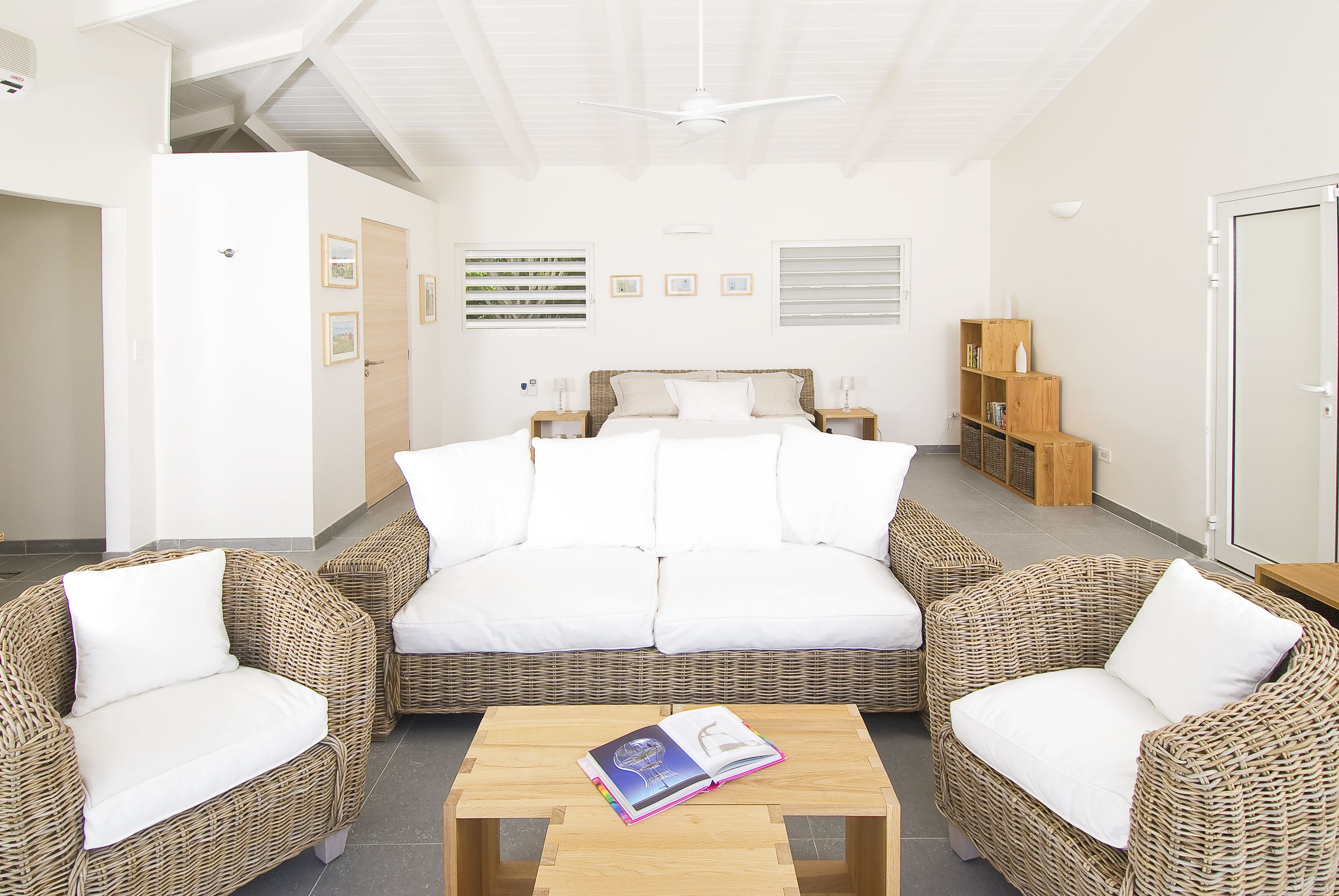 A bedroom with a large bed, two wicker sofas, a wooden coffee table, and a ceiling fan.
