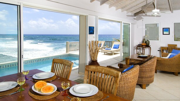 A dining area with a view of the ocean, a pool, and a balcony with wicker furniture. - Beach House Younes by Island Properties Online (Oyster Pond)