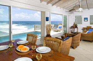 Un comedor con vista al océano, una piscina y un balcón con mobiliario de mimbre.