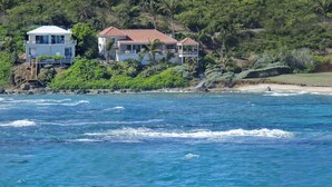 A coastal house with a balcony overlooking the sea, surrounded by lush greenery. - Beach House Younes by Island Properties Online (Oyster Pond)