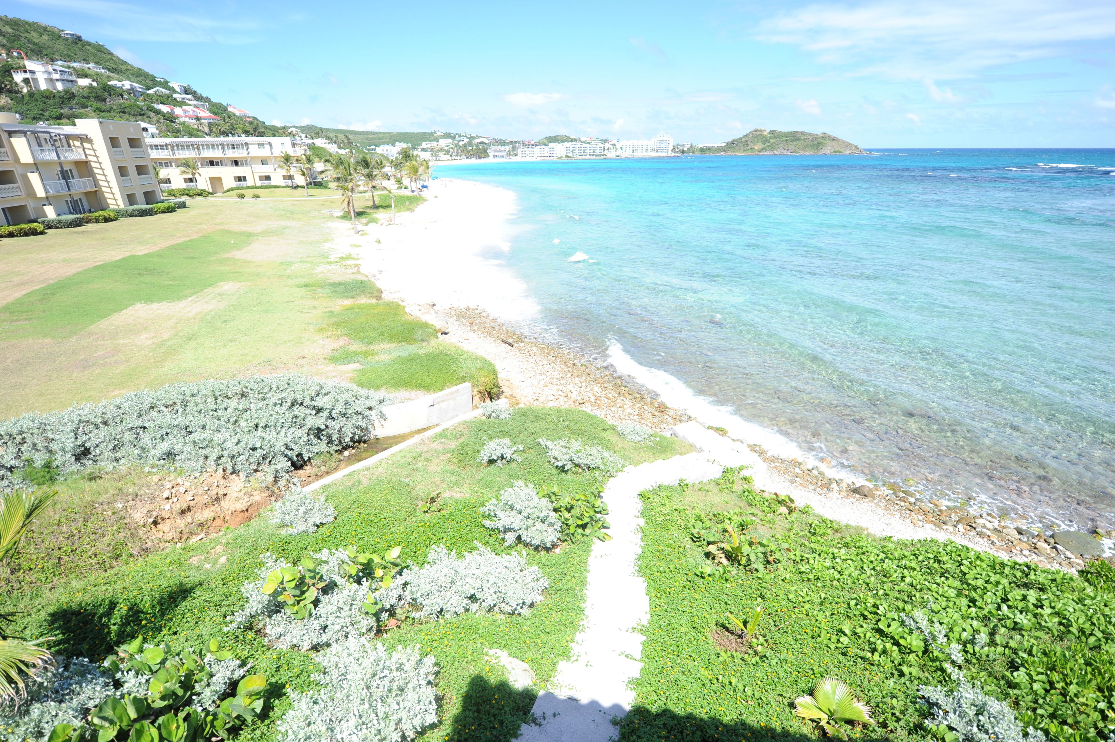 Hotel à beira-mar com vista para a praia, calçada pavimentada ao longo da costa e área de jardim ajardinada.
