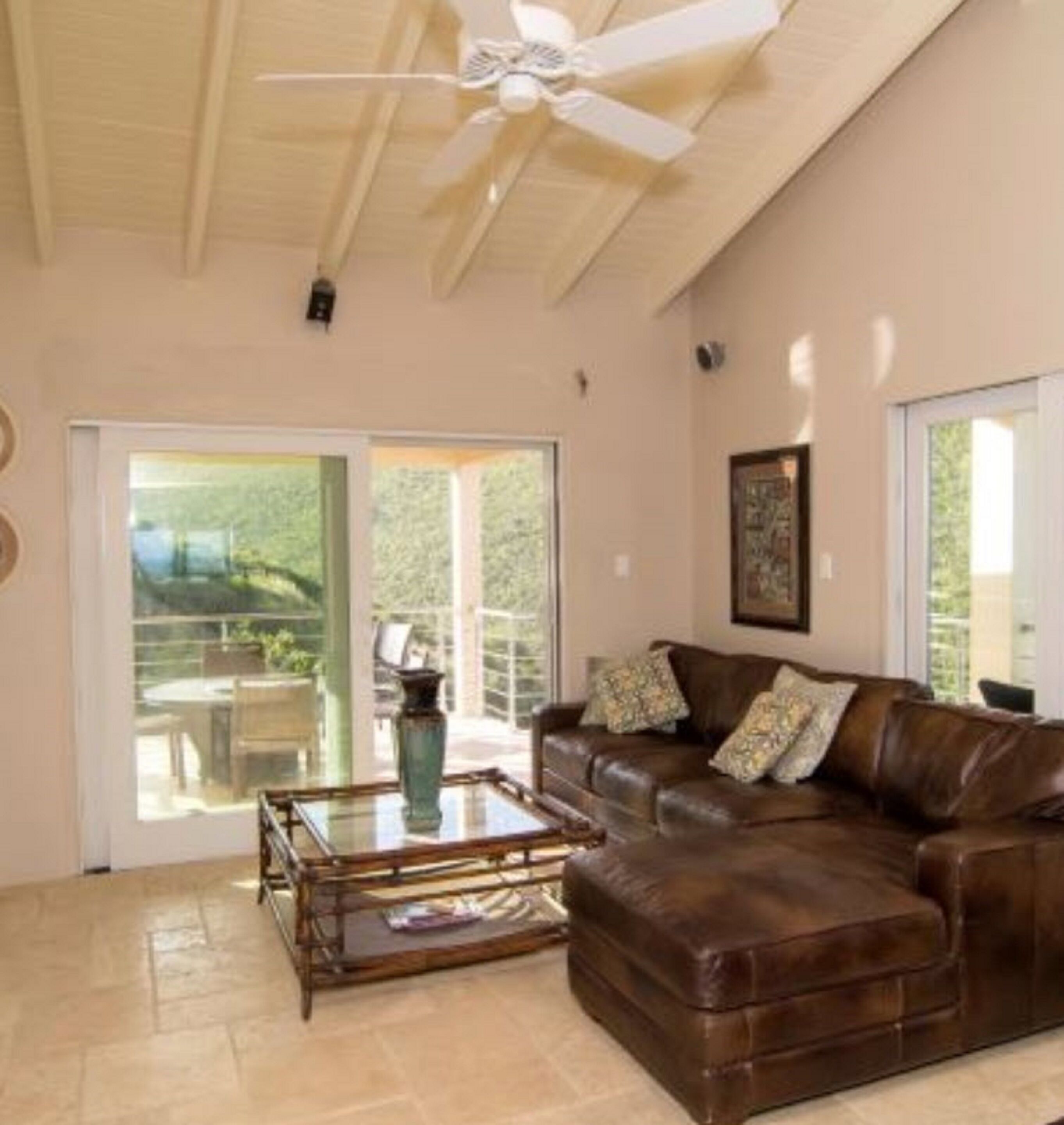 A spacious living room with a brown leather sofa, a glass coffee table, and a ceiling fan.