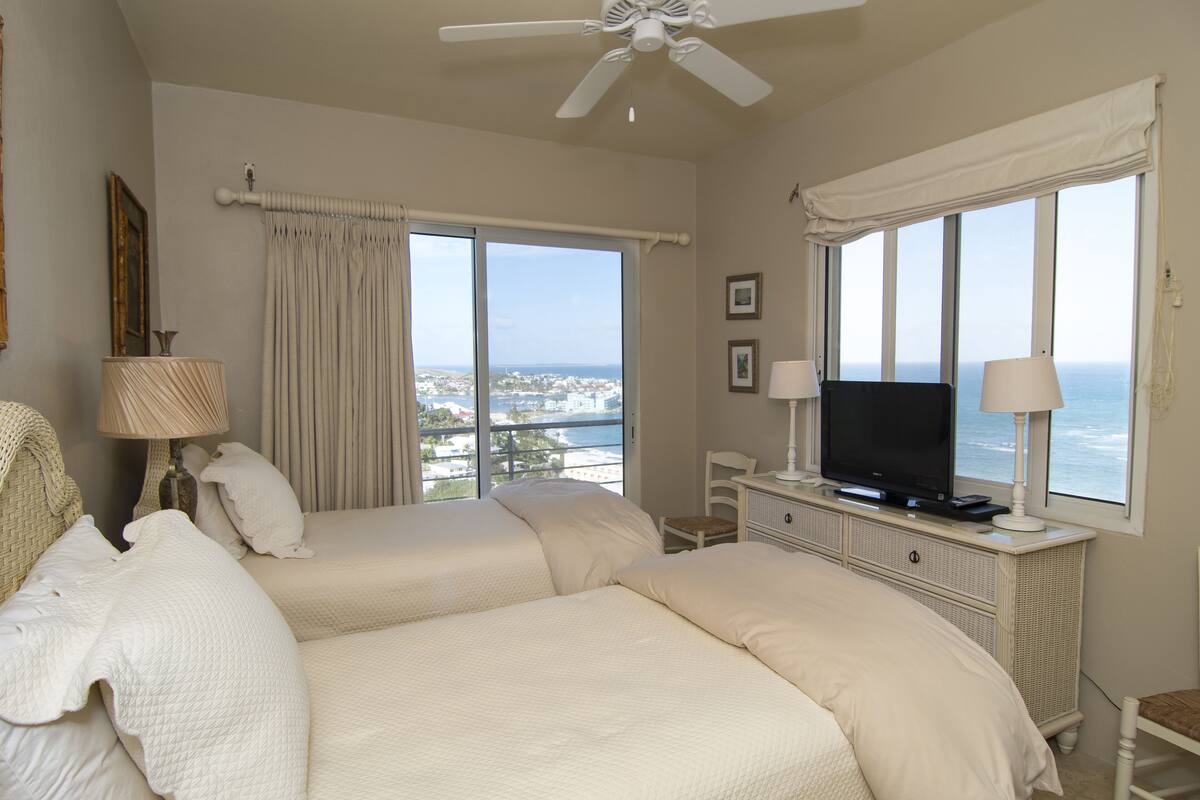 A hotel room with two beds, a television, a desk, and a view of the ocean.