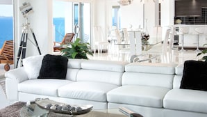 Uma sala de estar moderna com um sofá seccional branco, uma mesa de centro de vidro e vista para o oceano.