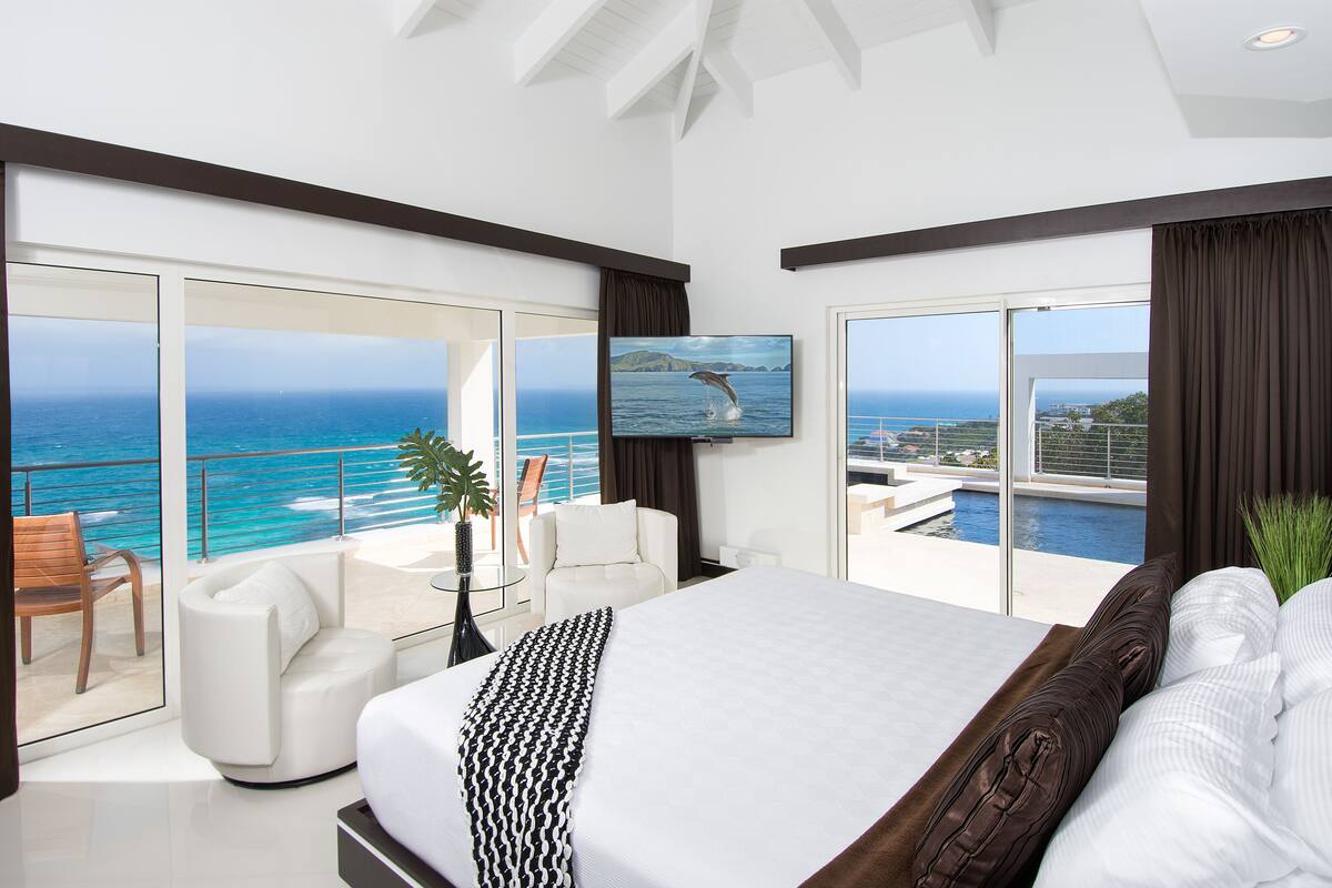 A modern hotel room with a large bed, a TV, and a balcony with a view of the ocean.