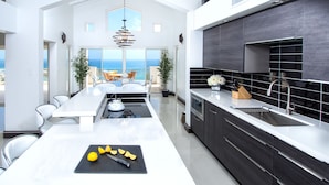 Cozinha moderna com ilha central, armários escuros e vista para o oceano.