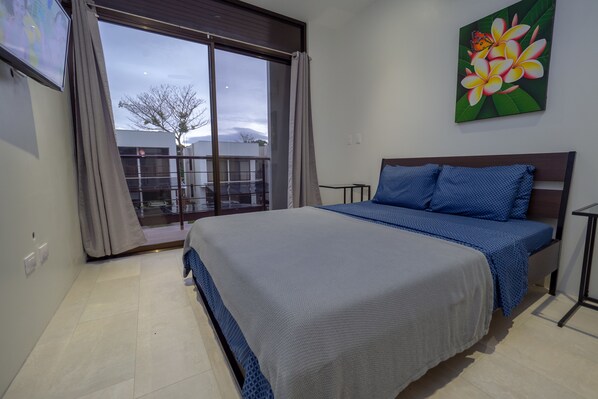 A bedroom with a large bed, a view through a sliding glass door, and a painting of flowers on the wall.