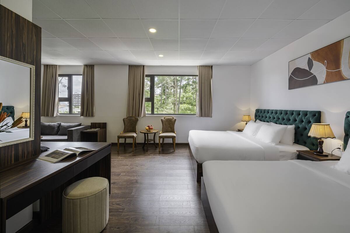 Habitación de hotel con dos camas, un escritorio, una silla, una mesita y una ventana con cortinas.