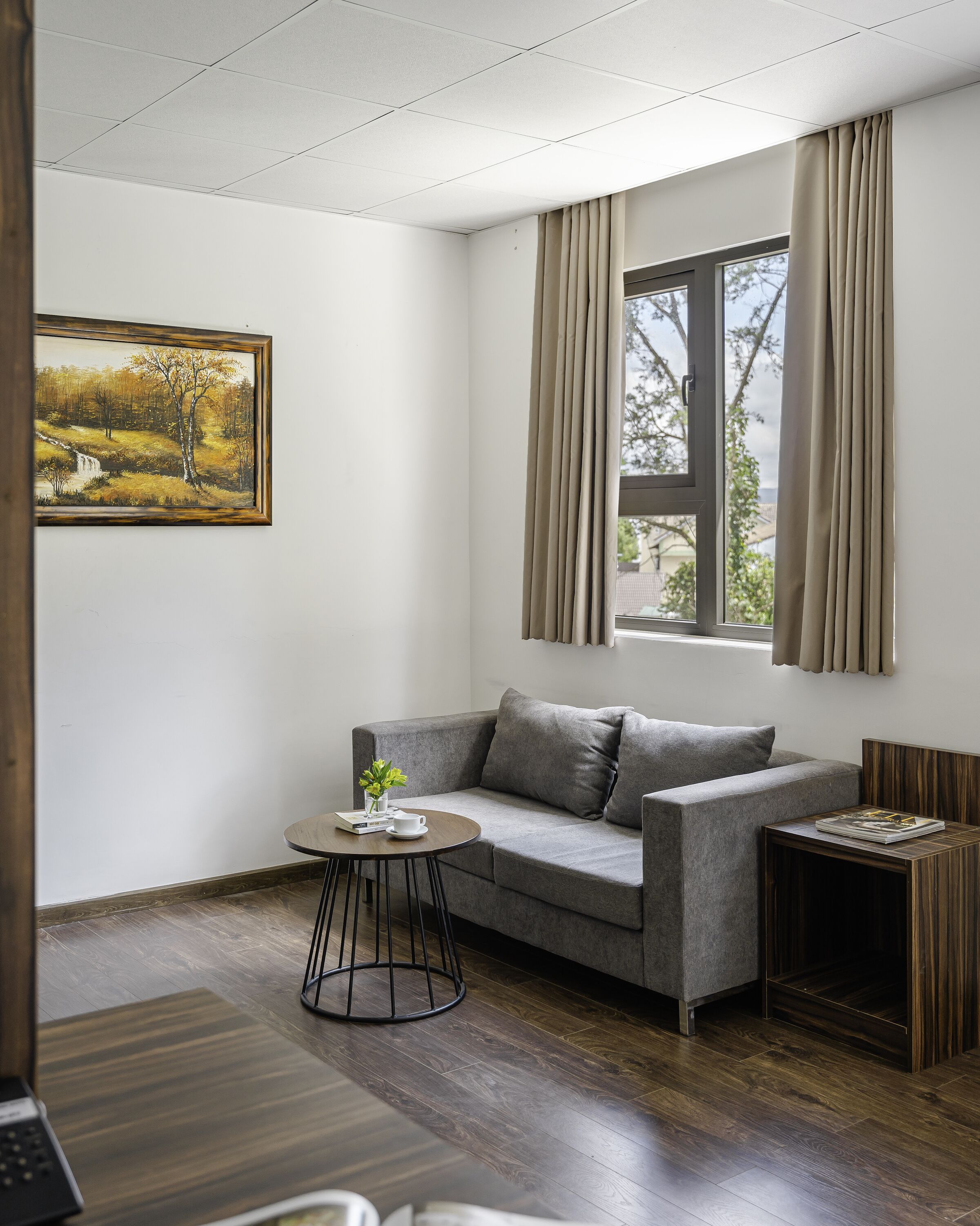 Una sala de estar moderna con un sofá gris, una mesa redonda de centro, una mesita de noche de madera y un cuadro en la pared.