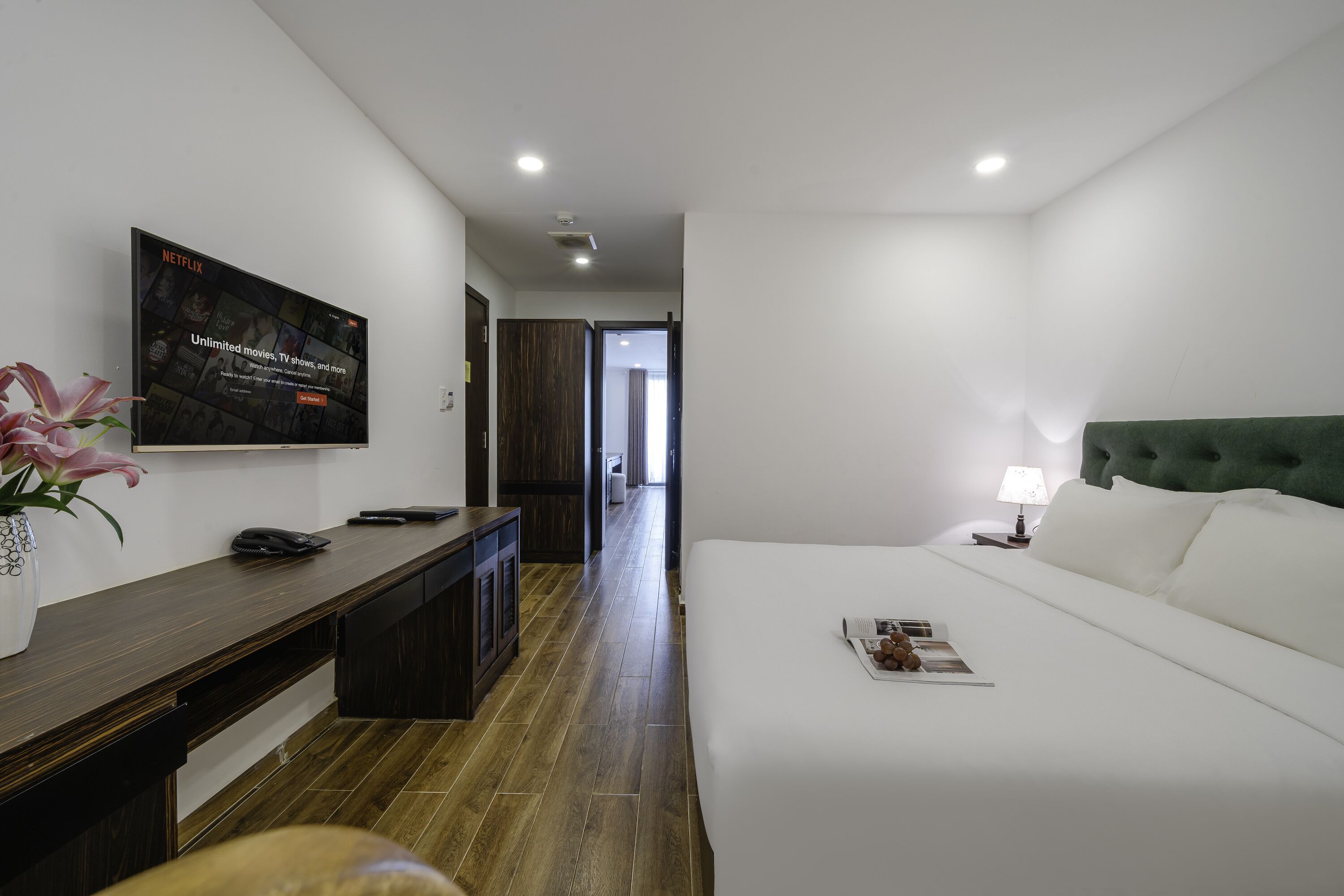 A hotel room with a bed, a desk with a phone, a TV displaying Netflix, and a lamp.
