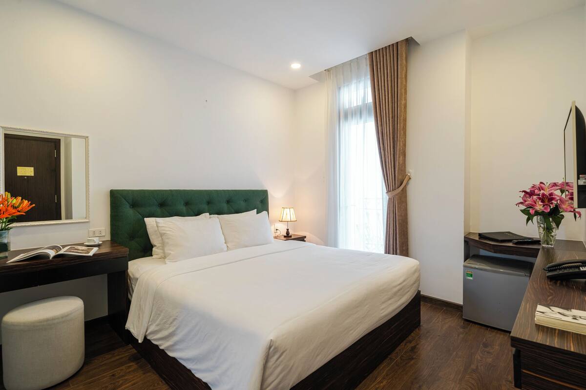 Una habitación de hotel con una cama grande, un escritorio con lámpara, un refrigerador pequeño y un espejo.