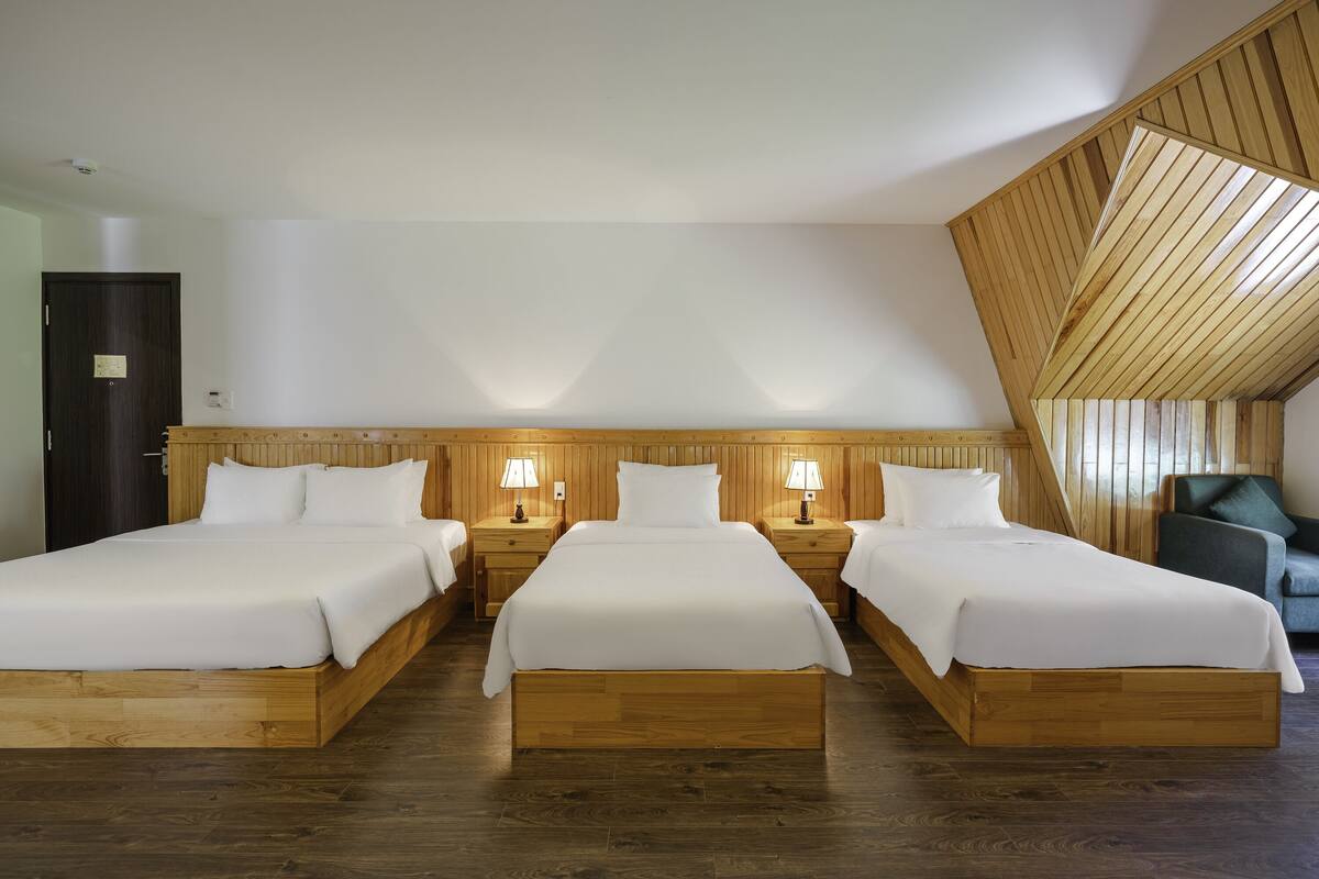 Habitación de hotel con tres camas de madera, cada una con una mesita de noche y lámpara a juego.