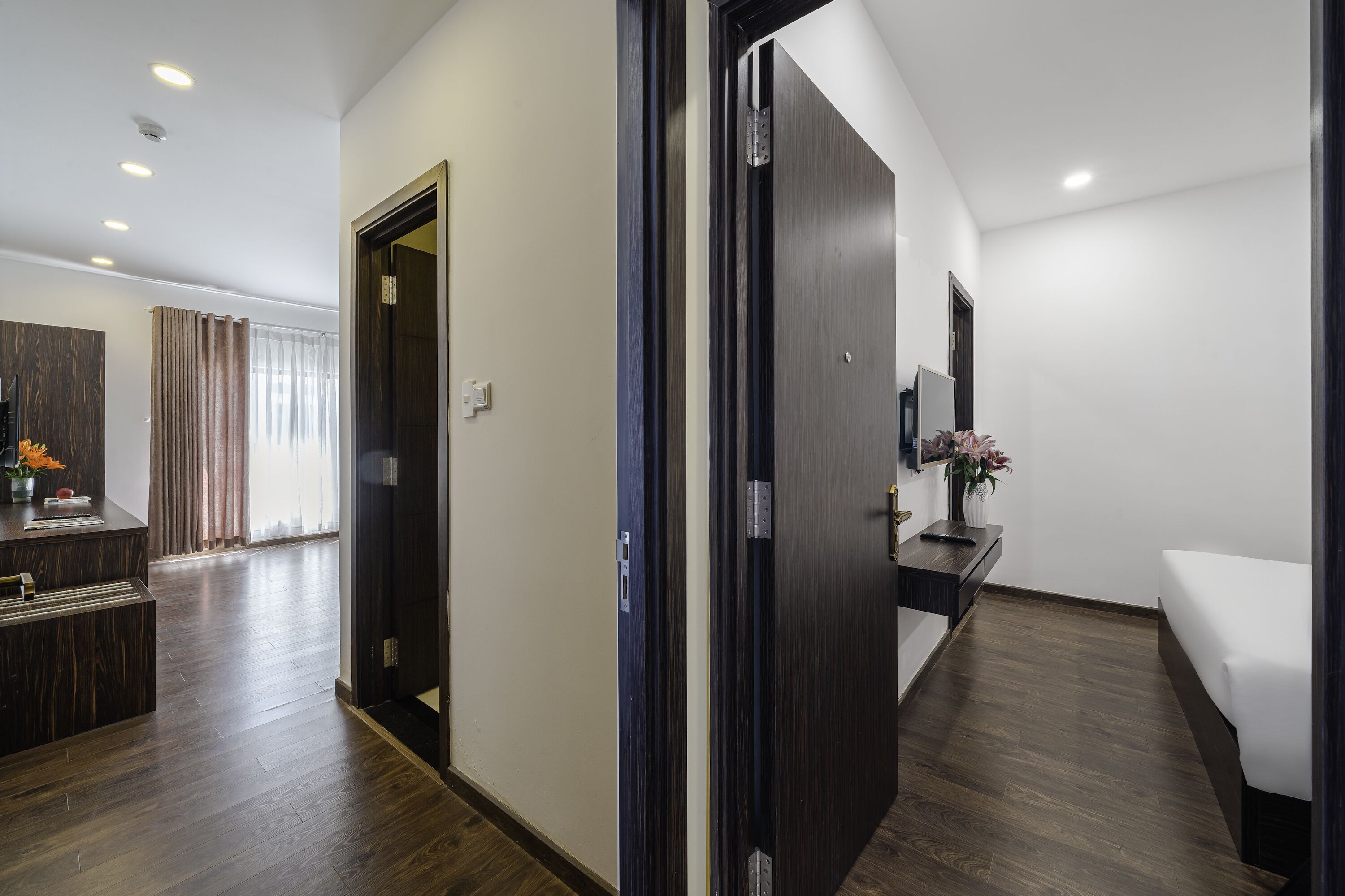 A hotel room with a wooden floor, a bed, a desk with a chair, a TV, and a bathroom with a mirror and sink.