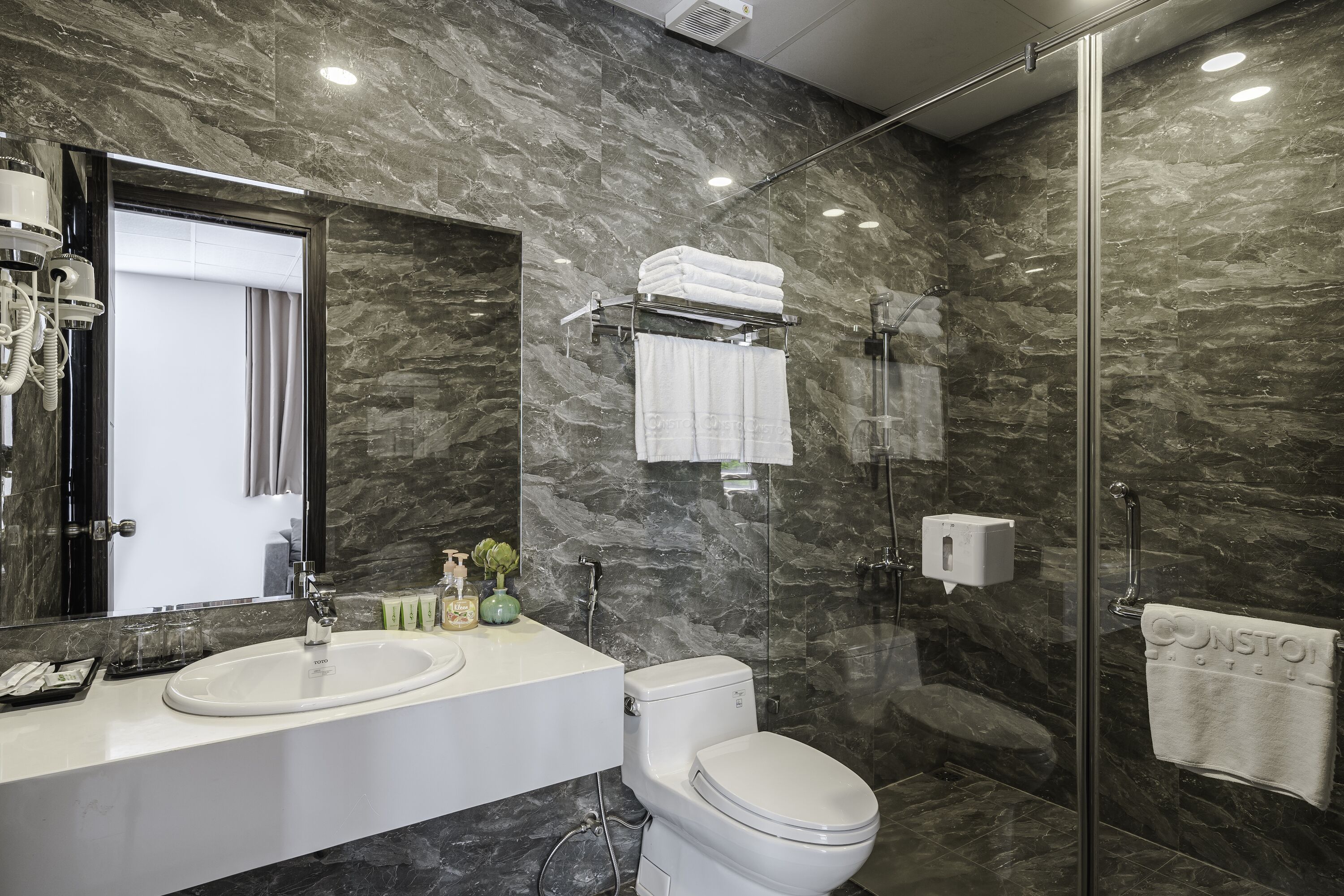Een moderne badkamer met een marmeren wand, een glazen douchecabine, een wit wastafelmeubel en een toilet.