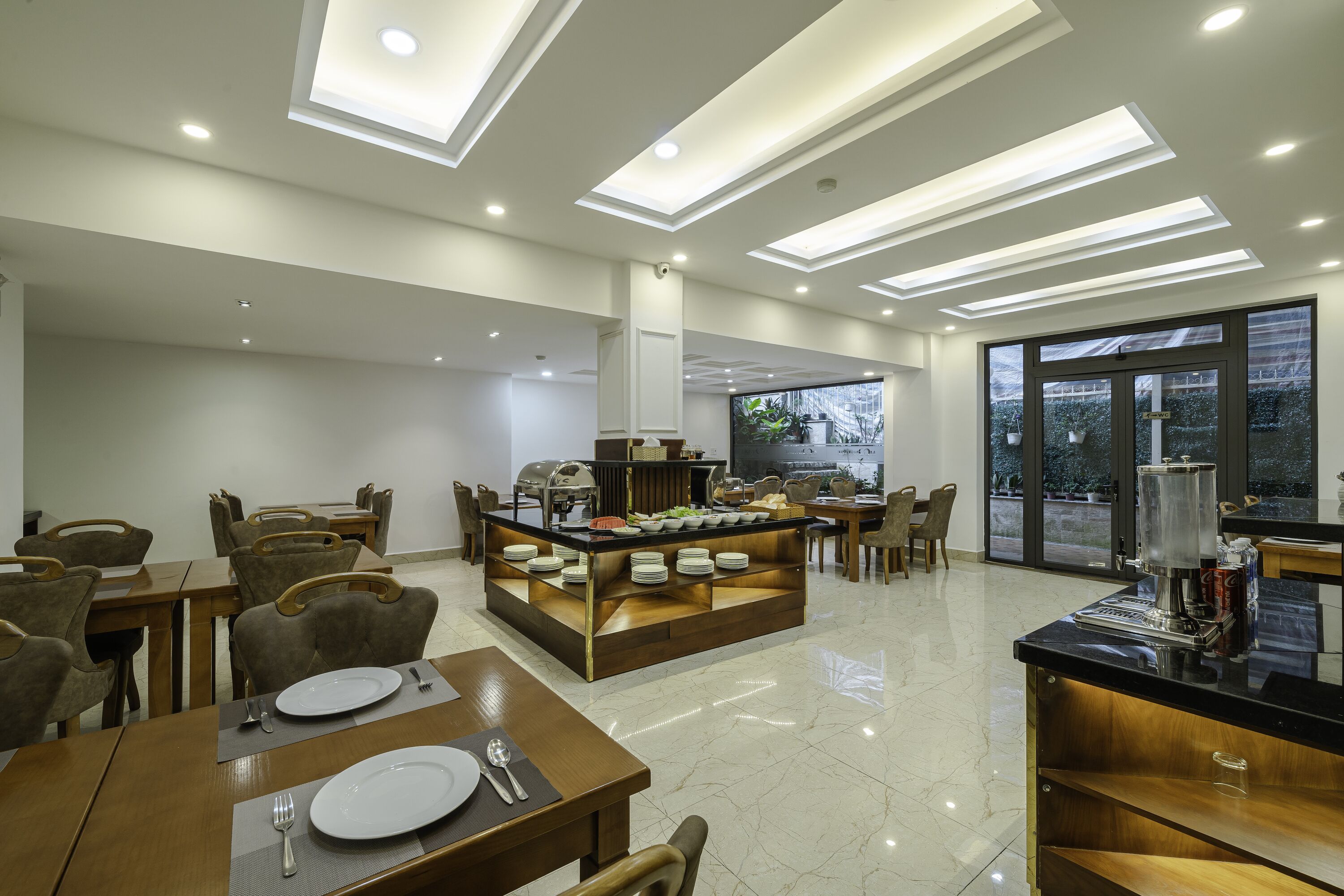 A modern dining area with a central buffet, multiple seating arrangements, and large windows providing natural light.