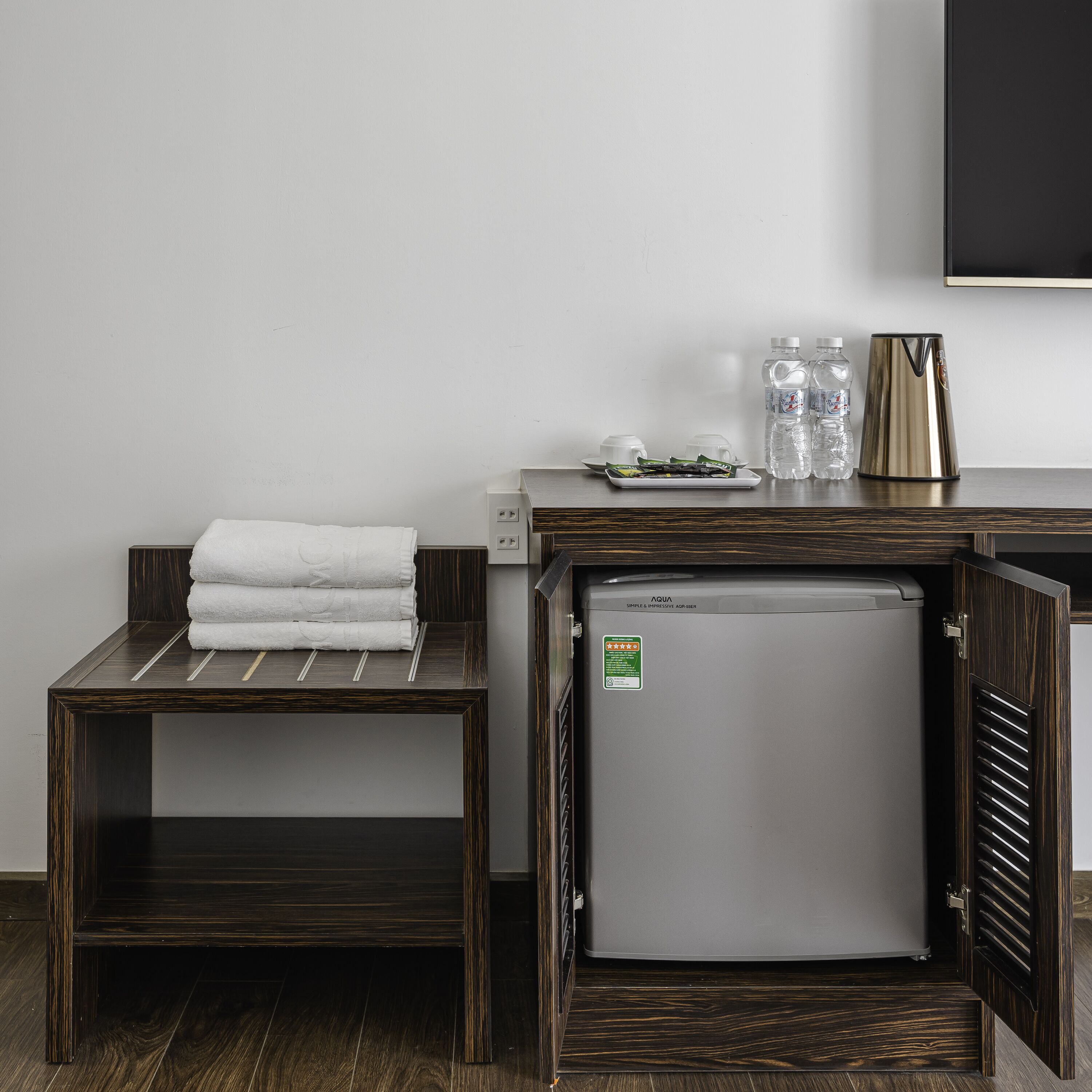 A compact kitchenette with a refrigerator, a small table with a towel, and a water dispenser.