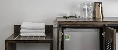 A compact kitchenette with a refrigerator, a small table with a towel, and a water dispenser.