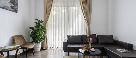 Una sala de estar moderna con un sofá seccional, una mesa de centro redonda, una planta en maceta y un cuadro en la pared.