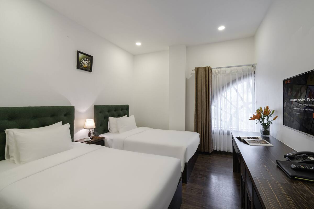 Habitación de hotel con dos camas, un escritorio con lámpara, televisión y ventana con cortinas.