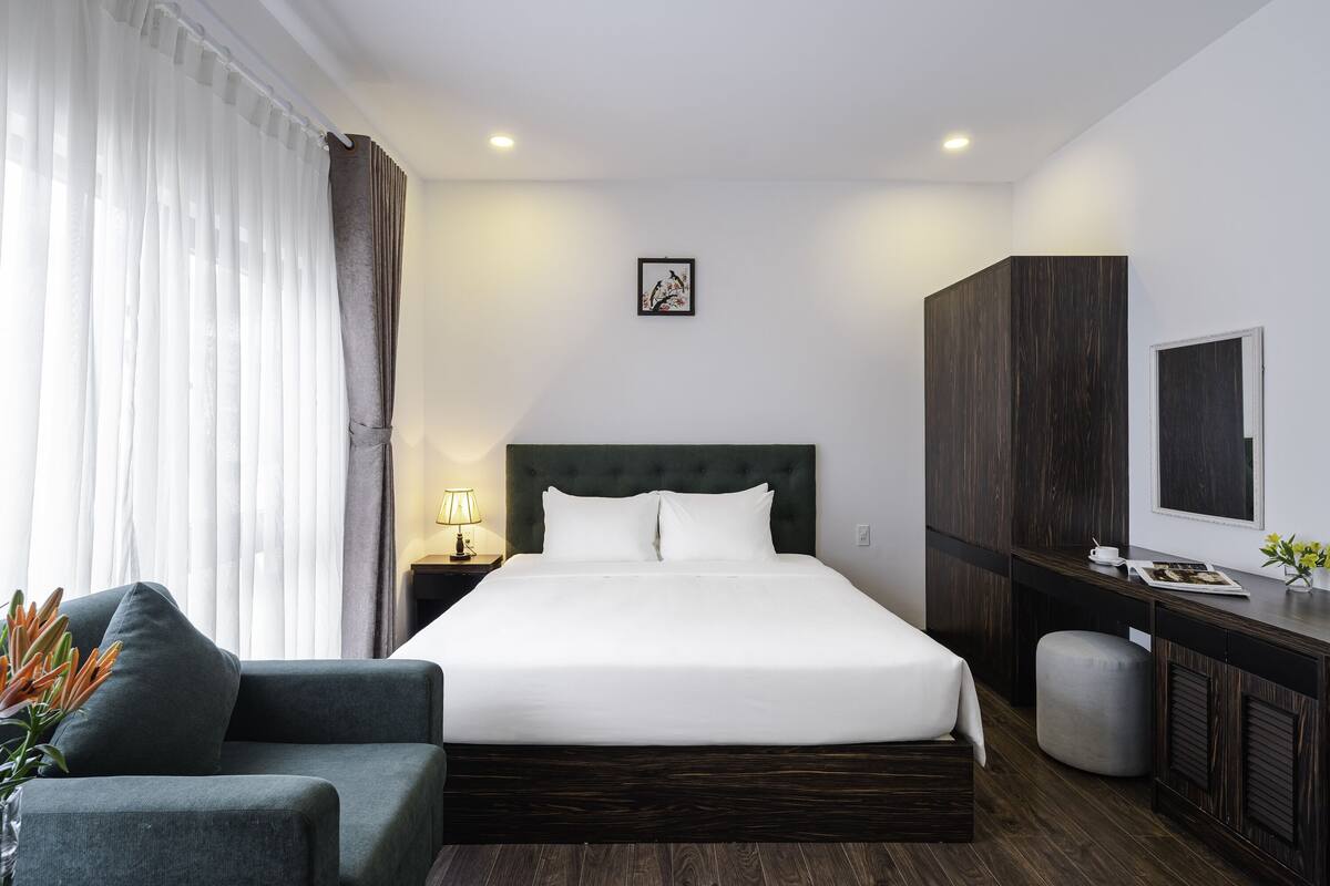 Una habitación de hotel moderna con una cama grande, un escritorio, una silla y una pequeña mesa con lámpara.
