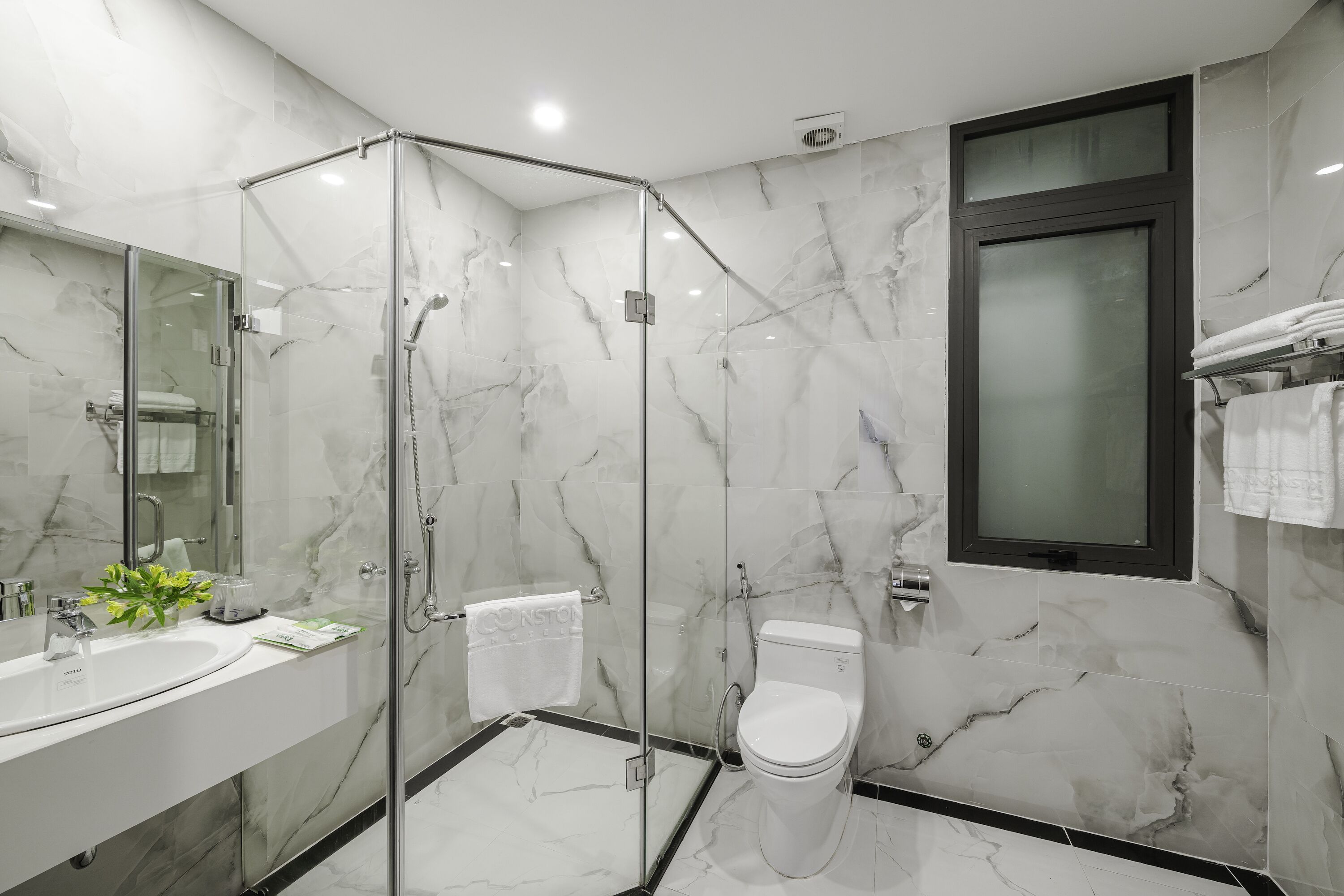 Ein modernes Badezimmer mit einer gläsernen Duschkabine, einem weißen Waschbecken und einer Toilette.