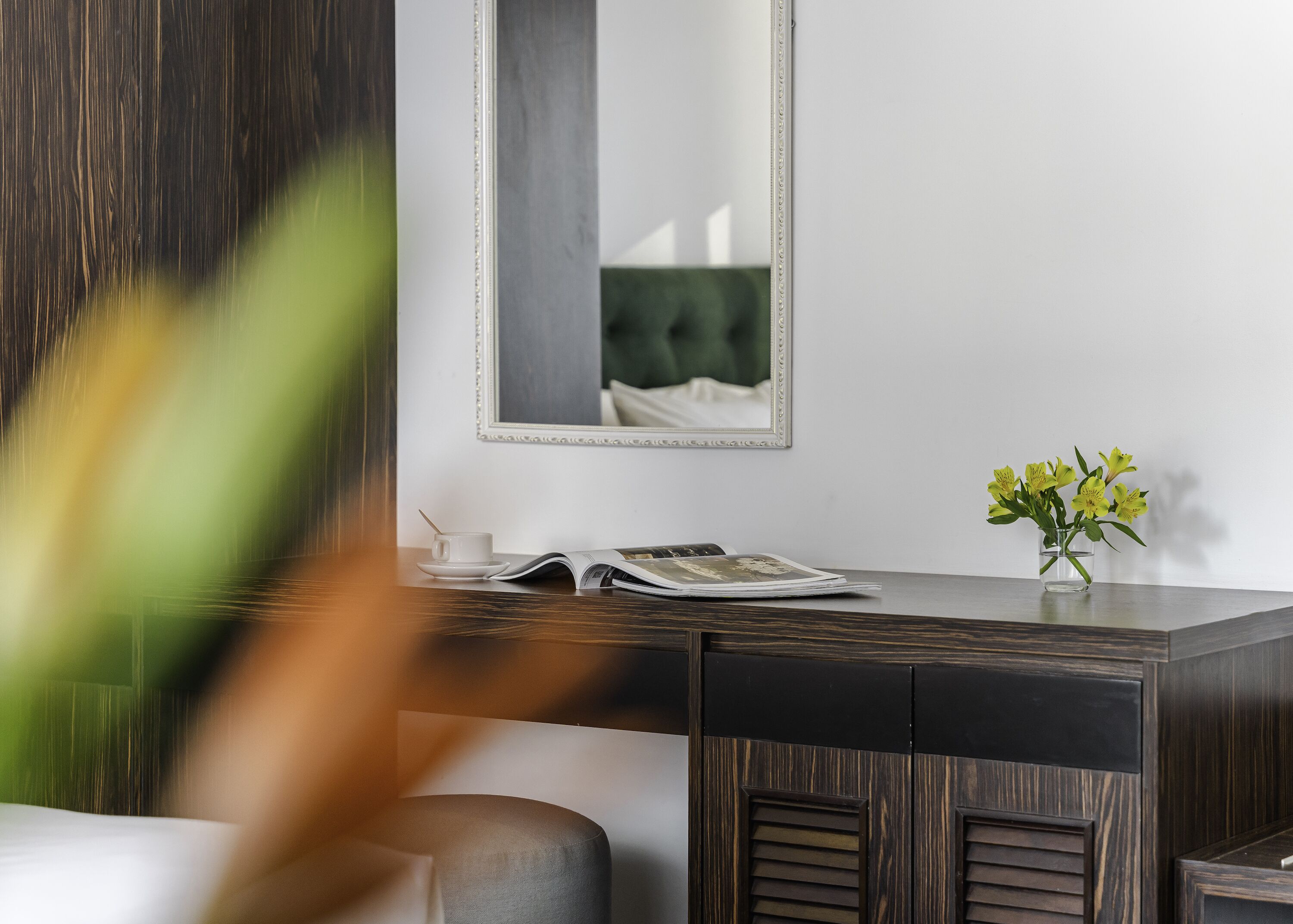 A modern room with a dark wooden desk, a white cup, a magazine, and a vase with yellow flowers.