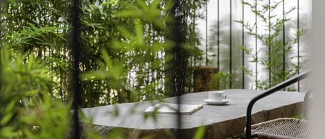 A stone table with a book and a cup, surrounded by greenery and a metal railing.