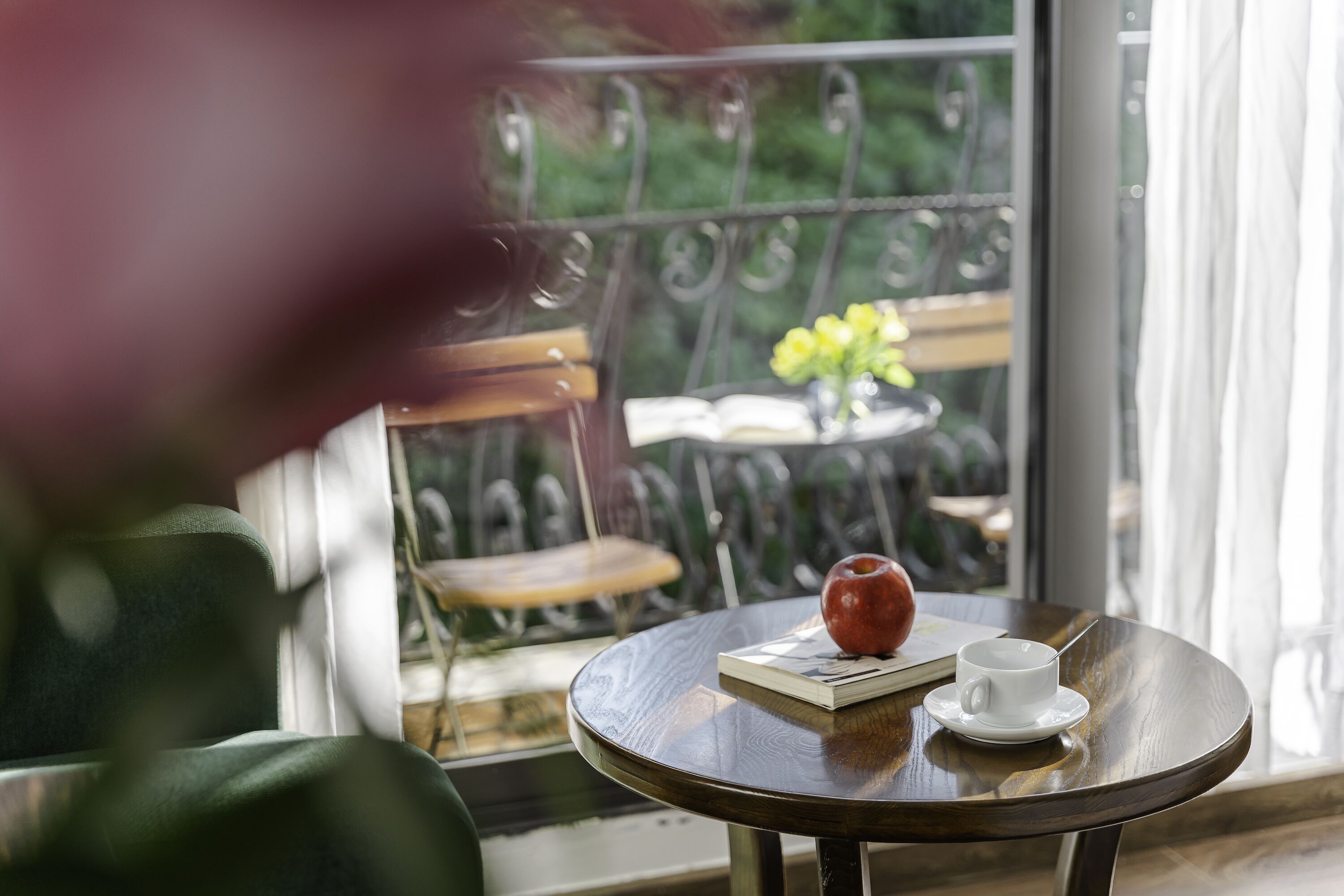 A round wooden table with a book, a white cup, and a red apple.