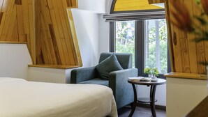 Une chambre d’hôtel moderne, équipée d’un lit, d’un canapé, d’une petite table avec une plante et d’une fenêtre donnant sur un paysage verdoyant.